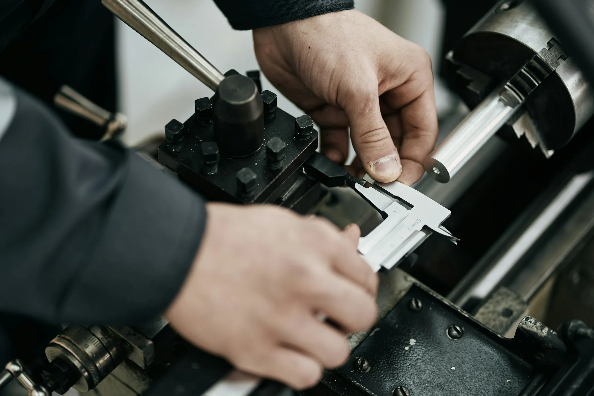 Mains d’un technicien mesurant une pièce au pied à coulisse sur un tour